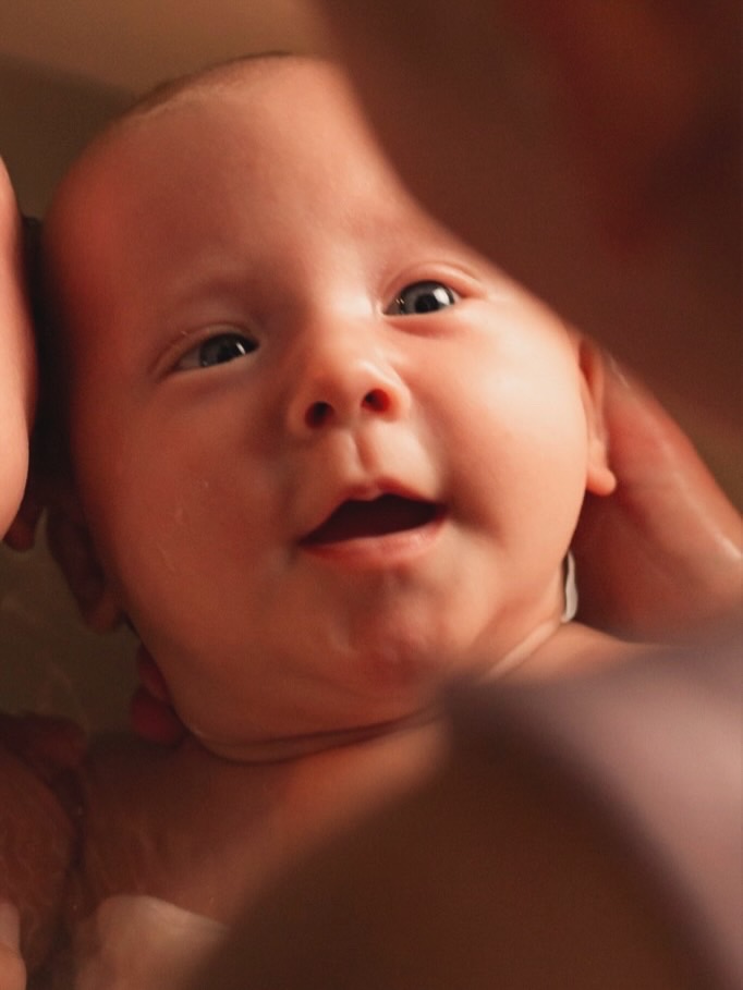 Bébé souriant, les yeux levés, la tête soutenue par des mains